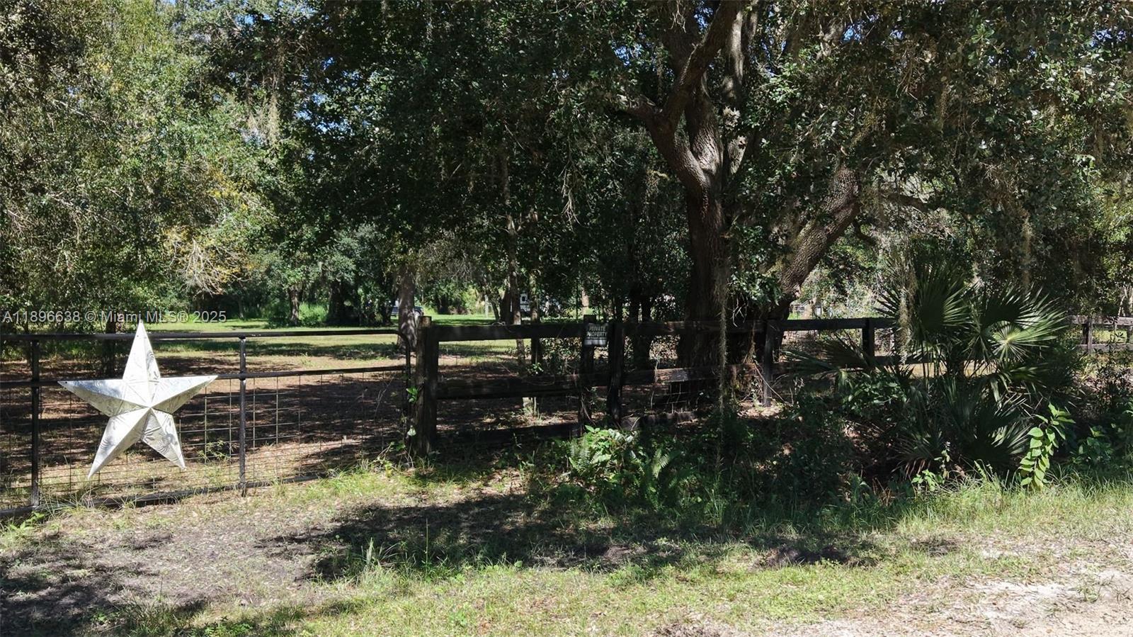 A metal star hangs on a wire fence bordering a wooded lot with trees — 20125 NW 300TH ST, Okeechobee FL 34972, OKEECHOBEE, FL