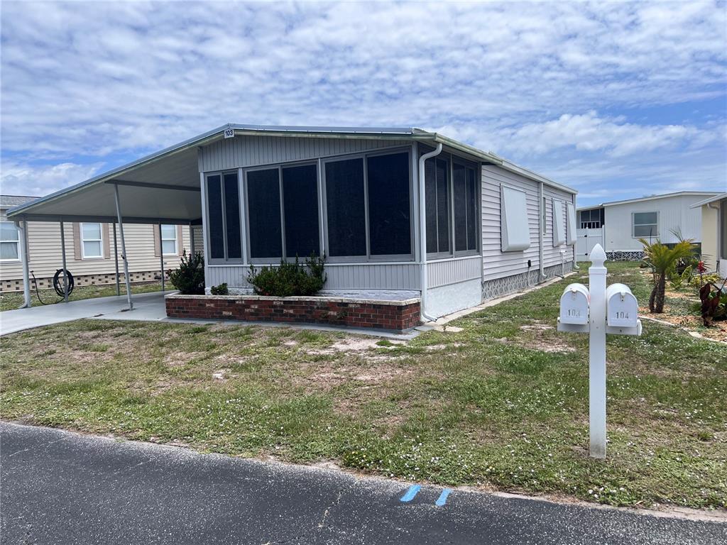 A light-colored mobile home features a screened-in porch, a carport, and a brick planter — 103 S FIJI CIRCLE, ENGLEWOOD, FL