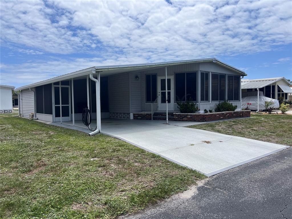 A light gray manufactured home features a carport, a screened porch, and a concrete driveway — 103 S FIJI CIRCLE, ENGLEWOOD, FL