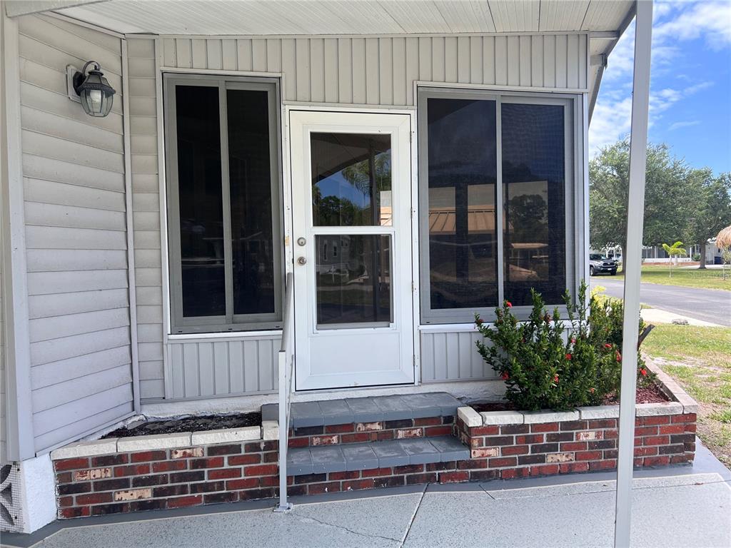 The exterior of a home features a white door, windows, and brick-bordered landscaping — 103 S FIJI CIRCLE, ENGLEWOOD, FL