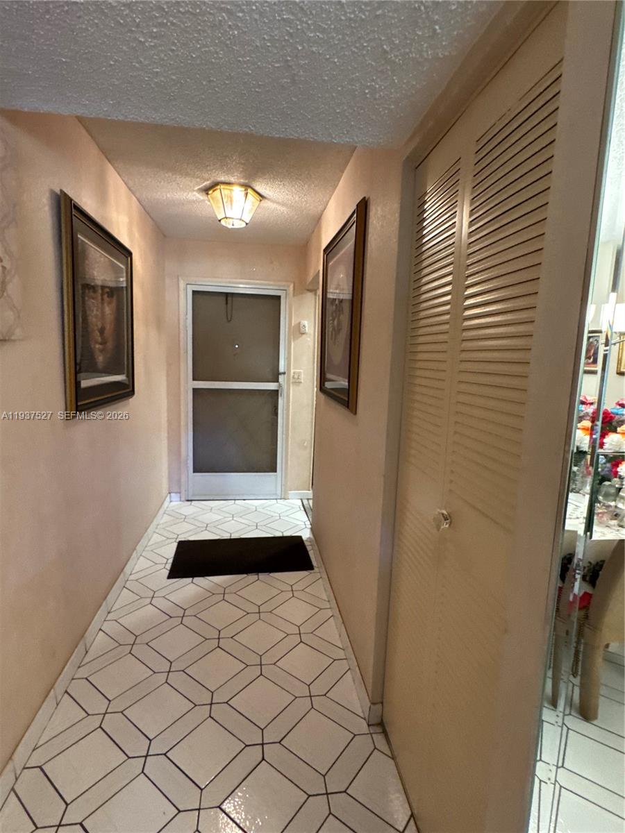 A hallway features light-colored walls, framed artwork, a louvered closet door, and geometric floor tiles — 6080 NW 44th St # 107, Lauderhill FL 33319, LAUDERHILL, FL