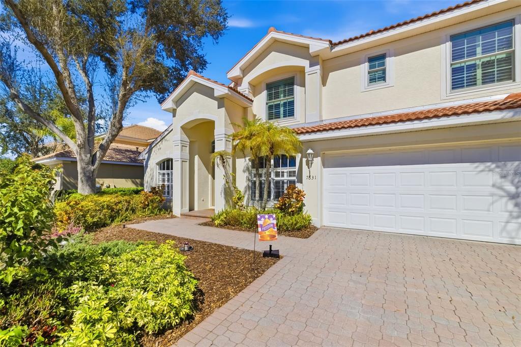 A two-story suburban house with a beige stucco exterior, tile roof, and paved driveway — 7631 DESERT INN WAY, LAKEWOOD RANCH, FL