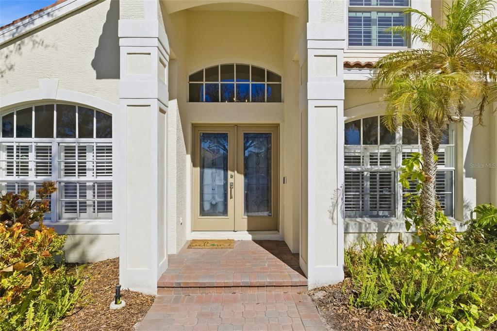 A beige house exterior features a brick walkway leading to double glass front doors — 7631 DESERT INN WAY, LAKEWOOD RANCH, FL