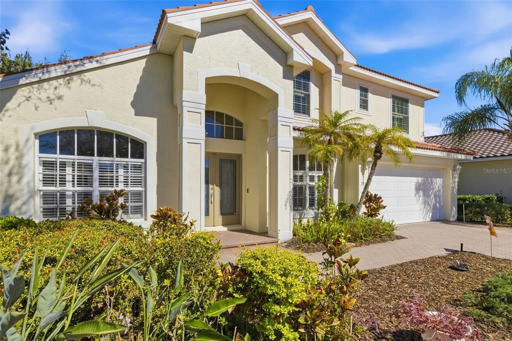 A two-story house with a beige stucco exterior, arched entryway, and a paved driveway — 7631 DESERT INN WAY, LAKEWOOD RANCH, FL