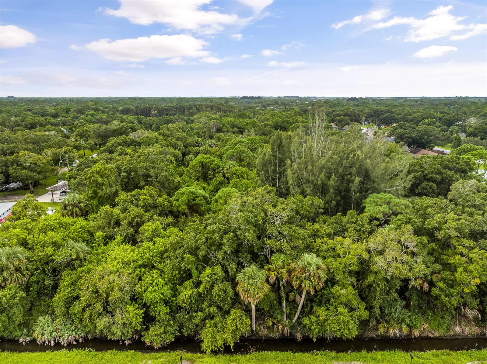 An aerial view shows a dense forest bordering a narrow canal under a cloudy sky — 6145 45th Street, Vero Beach FL 32967, VERO BEACH, FL