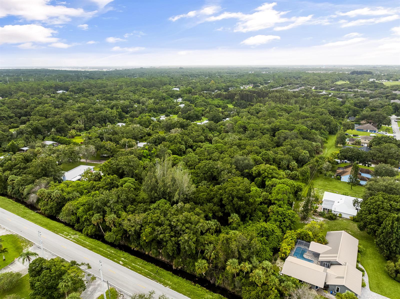 An aerial view shows a residential neighborhood surrounded by dense forest and a paved road — 6145 45th Street, Vero Beach FL 32967, VERO BEACH, FL