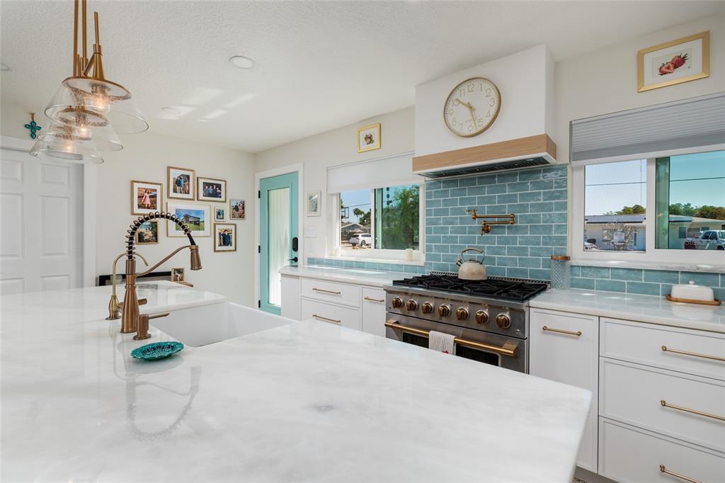 A kitchen features white cabinets, marble countertops, a blue tiled backsplash, and a gas range — 9298 SUN ISLE DRIVE NE, ST PETERSBURG, FL