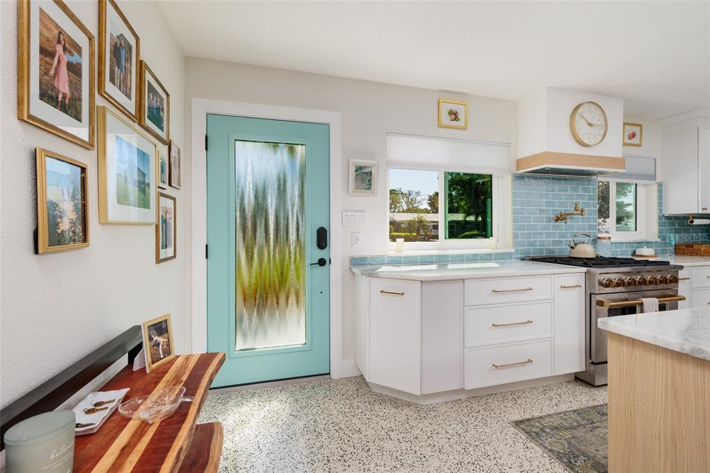 A kitchen features a light blue door, white cabinets, a tiled backsplash, and terrazzo flooring — 9298 SUN ISLE DRIVE NE, ST PETERSBURG, FL