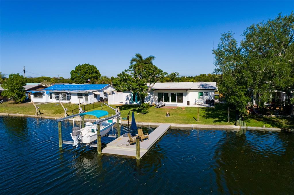 A waterfront house with a boat lift and dock sits on a grassy lawn — 9298 SUN ISLE DRIVE NE, ST PETERSBURG, FL