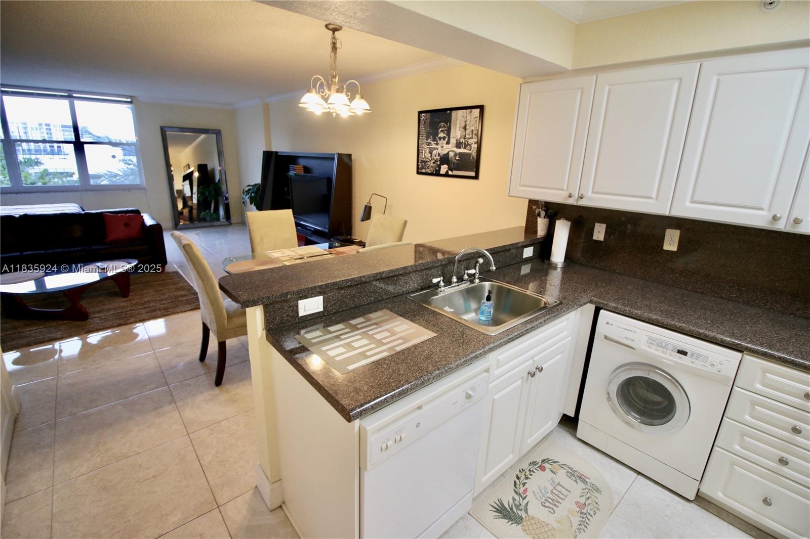 A kitchen with white cabinets and dark countertops overlooks a living and dining area — 2501 S Ocean Dr # 427, Hollywood FL 33019, HOLLYWOOD, FL