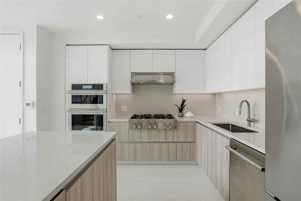 A modern kitchen features white upper cabinets, wood-grain lower cabinets, stainless steel appliances, and countertops — 400 CENTRAL AVENUE UNIT 306, ST PETERSBURG, FL