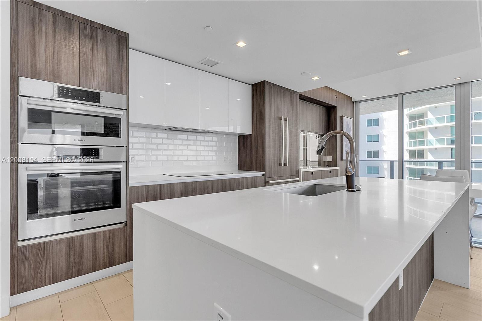 A modern kitchen features white countertops, dark wood cabinetry, stainless steel appliances, and floor-to-ceiling windows — 488 NE 18th St # 2315, Miami FL 33132, MIAMI, FL