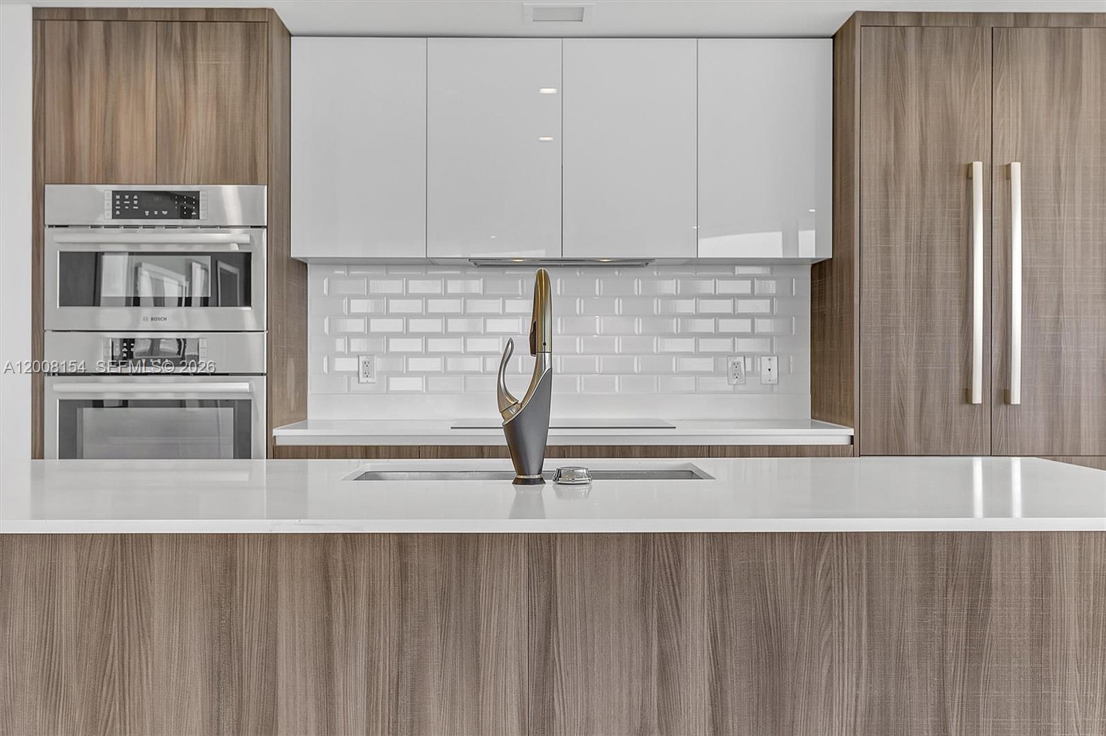 A modern kitchen features wood-grain cabinetry, white upper cabinets, a white island, and subway tile — 488 NE 18th St # 2315, Miami FL 33132, MIAMI, FL