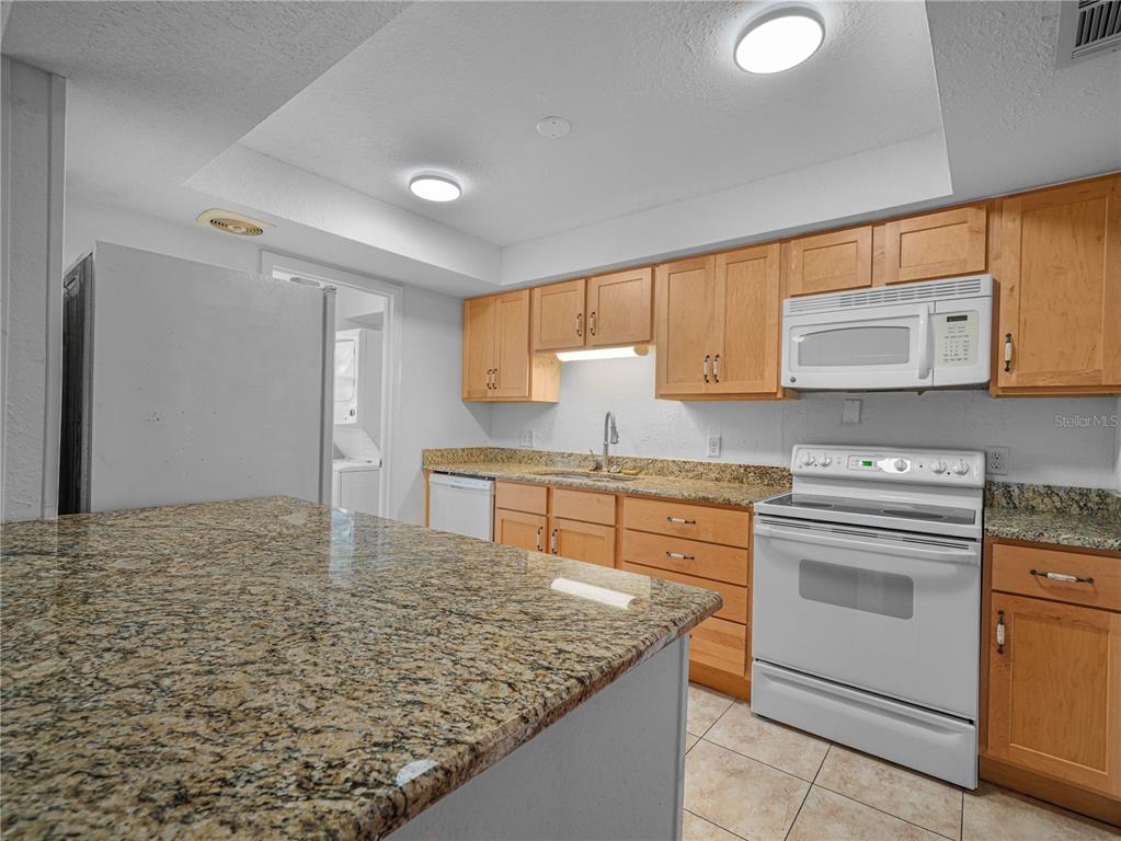 A kitchen features light wood cabinets, granite countertops, white appliances, and a breakfast bar — 1130 N LAKE PARKER AVENUE UNIT A301, LAKELAND, FL