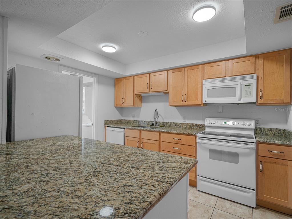 A kitchen features light wood cabinets, granite countertops, and white appliances — 1130 N LAKE PARKER AVENUE UNIT A301, LAKELAND, FL