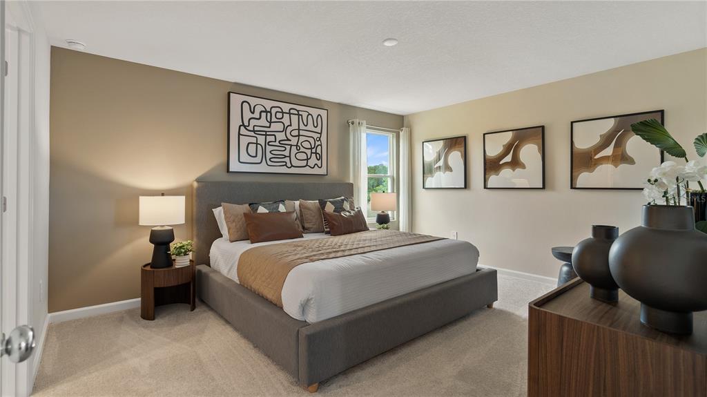 A bedroom features a gray upholstered bed, neutral walls, modern artwork, and a bedside lamp — 2477 HALLOW GARDEN ROAD, EUSTIS, FL