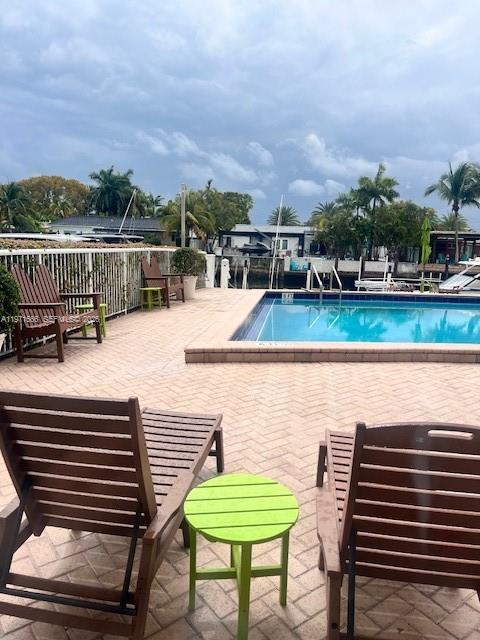 A patio with lounge chairs and a small table overlooks a swimming pool and canal — 2000 NE 135th St # 601, North Miami FL 33181, NORTH MIAMI, FL