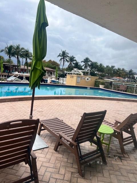 A patio with lounge chairs and a closed umbrella overlooks a swimming pool and canal — 2000 NE 135th St # 601, North Miami FL 33181, NORTH MIAMI, FL