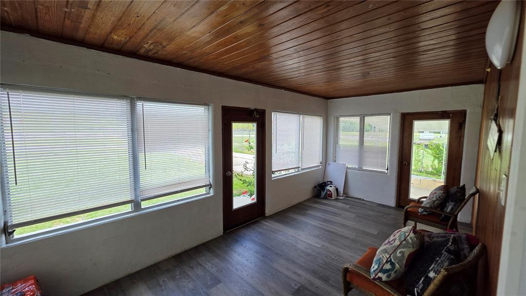 A sunroom with wood-paneled ceiling, gray flooring, multiple windows, and two wicker chairs — 13330 FORT KING ROAD, DADE CITY, FL