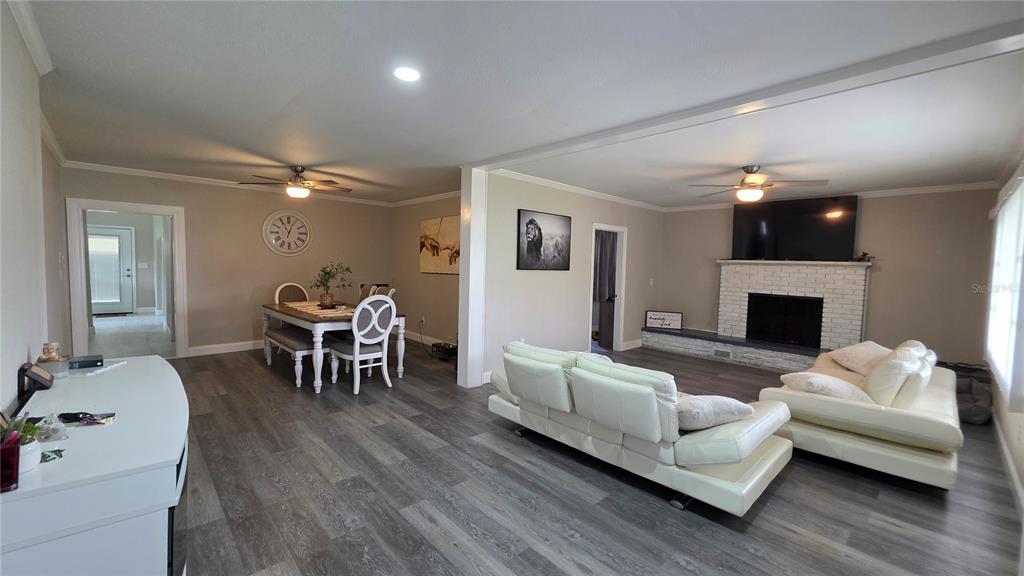 An open-concept living and dining area features gray wood-look flooring, white furniture, and a fireplace — 13330 FORT KING ROAD, DADE CITY, FL