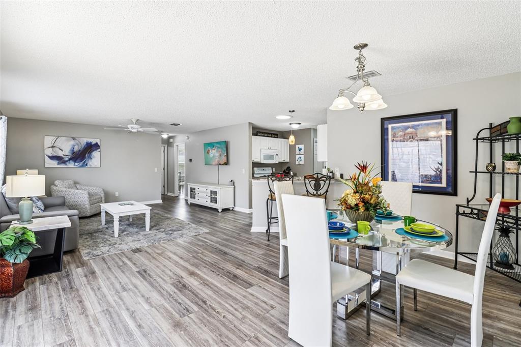 An open-concept living and dining area features gray wood-look flooring and a white kitchen — 2561 BIRCH AVENUE, THE VILLAGES, FL