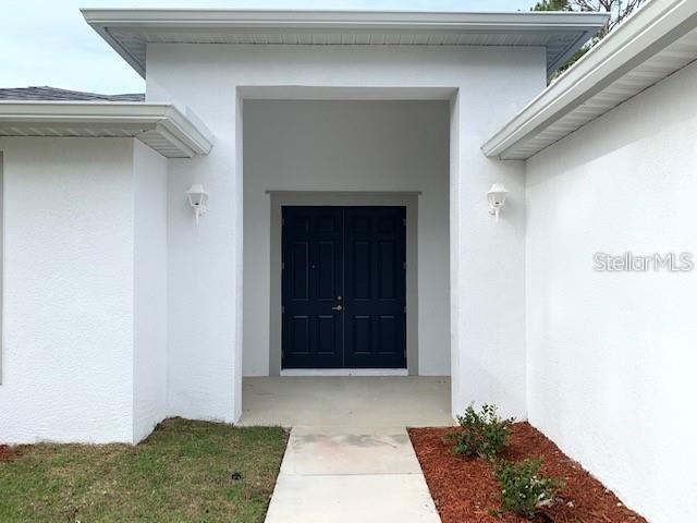 The exterior of a white house features a recessed entryway with dark double doors — 1455 HARBELL STREET, NORTH PORT, FL