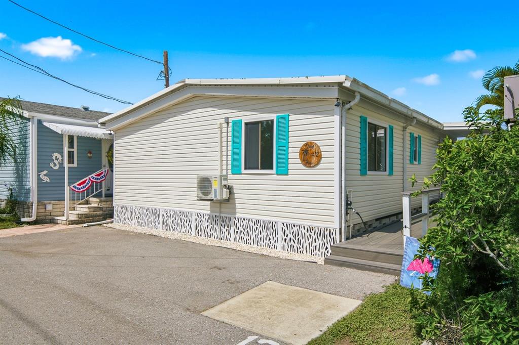A light-colored mobile home with turquoise shutters and a small deck sits on a lot — 15010 113TH AVENUE UNIT 12, LARGO, FL