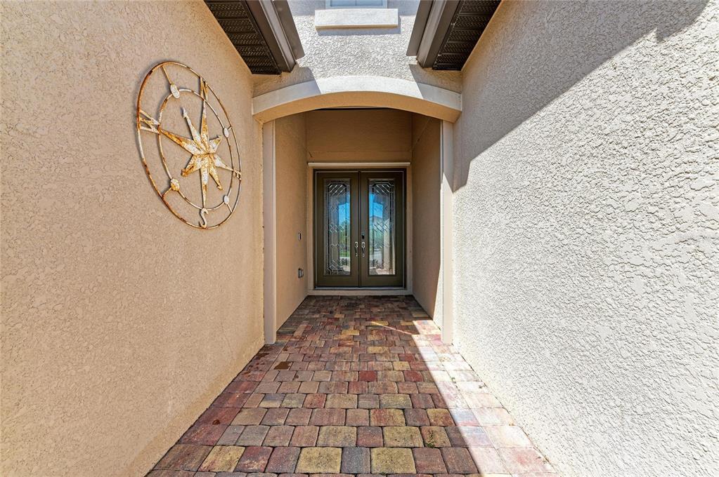 A covered entryway features a brick paver walkway, a compass wall decoration, and double doors — 20706 BENISSIMO DRIVE, VENICE, FL