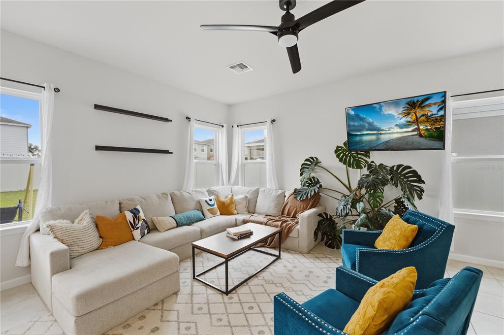 A living room features a large sectional sofa, two blue armchairs, and a wall-mounted television — 1715 OCEANIA AVENUE, DAVENPORT, FL