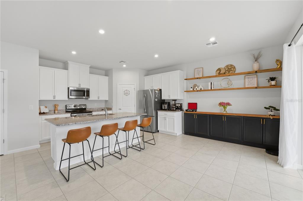 A kitchen features white cabinetry, a granite-topped island with bar stools, and dark lower cabinets — 1715 OCEANIA AVENUE, DAVENPORT, FL