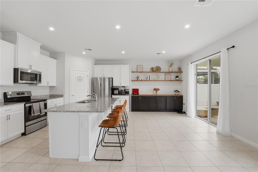 A kitchen features white cabinets, a granite-topped island with bar stools, and dark lower cabinetry — 1715 OCEANIA AVENUE, DAVENPORT, FL