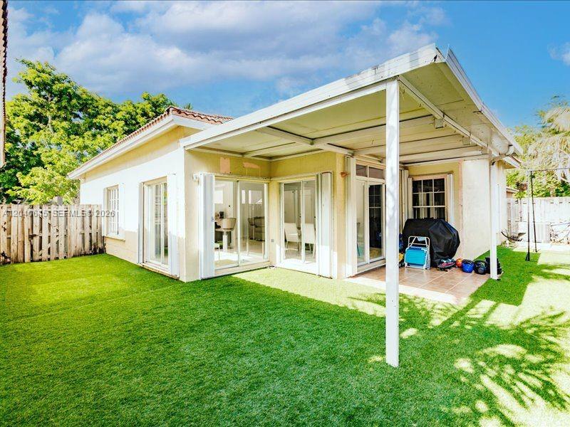 A backyard with artificial turf, a covered patio, and sliding glass doors leading into a house — 21475 SW 90th Pl, Cutler Bay FL 33189, CUTLER BAY, FL