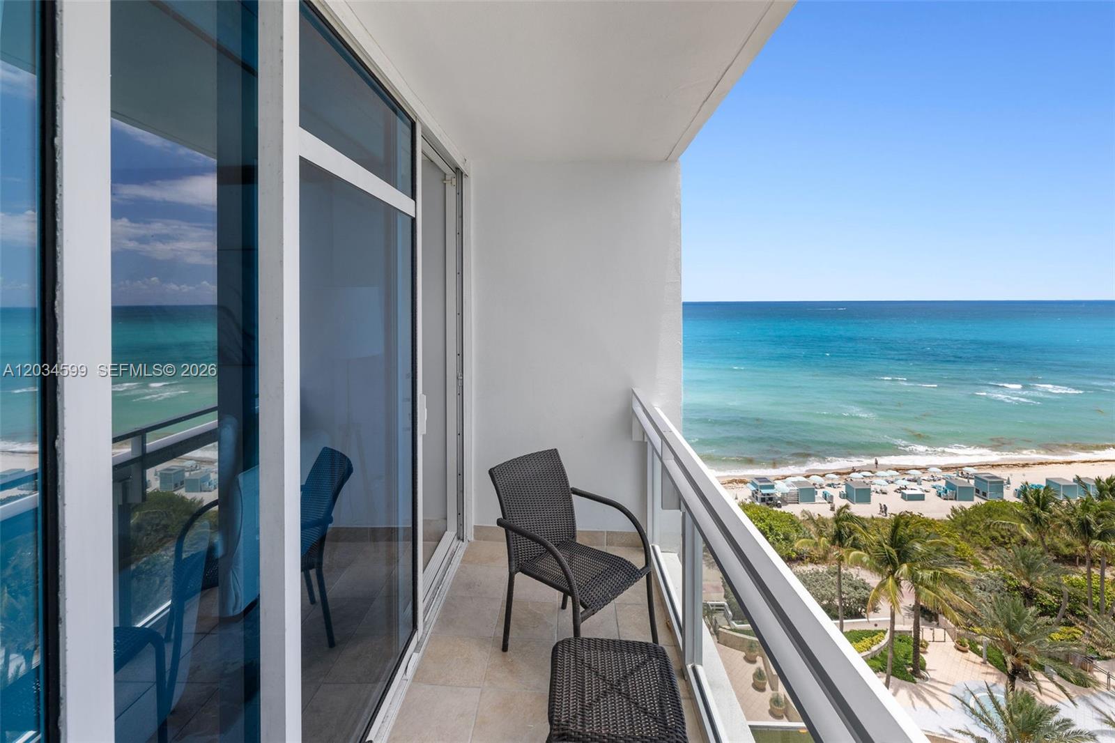 A balcony with a chair and ottoman overlooks the ocean and a sandy beach — 6801 Collins Ave # 1010, Miami Beach FL 33141, MIAMI BEACH, FL