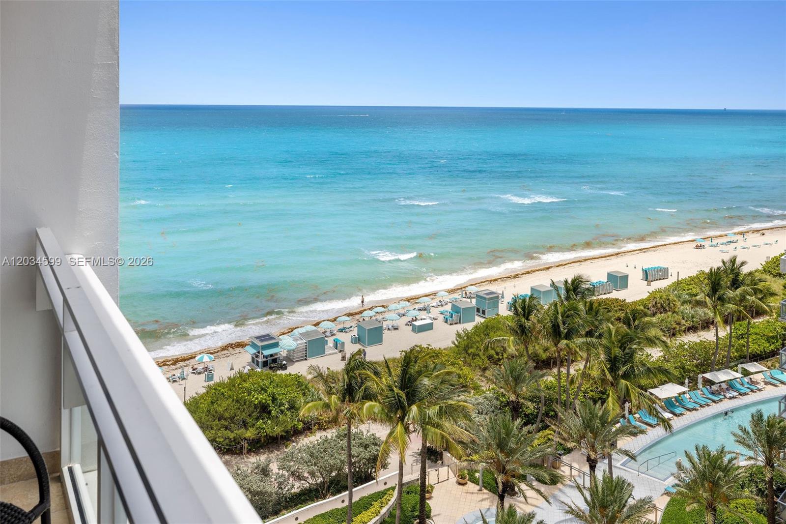 An elevated view from a balcony overlooks a sandy beach, ocean, and swimming pool — 6801 Collins Ave # 1010, Miami Beach FL 33141, MIAMI BEACH, FL