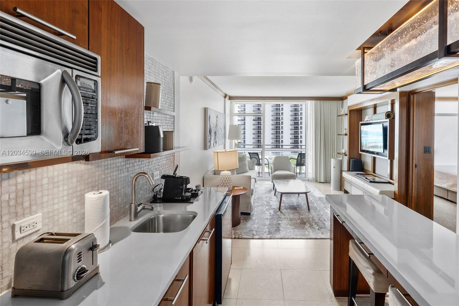 A kitchen with wood cabinets and white countertops opens into a living area with balcony access — 6801 Collins Ave # 1010, Miami Beach FL 33141, MIAMI BEACH, FL