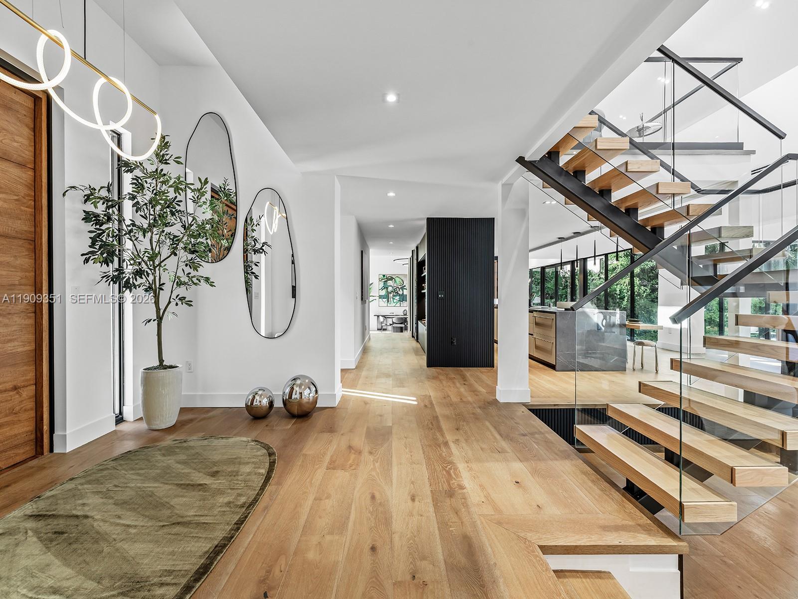 A modern entryway features light wood floors, a floating staircase, and two oval wall mirrors — 7910 Los Pinos Cir, Coral Gables FL 33143, CORAL GABLES, FL