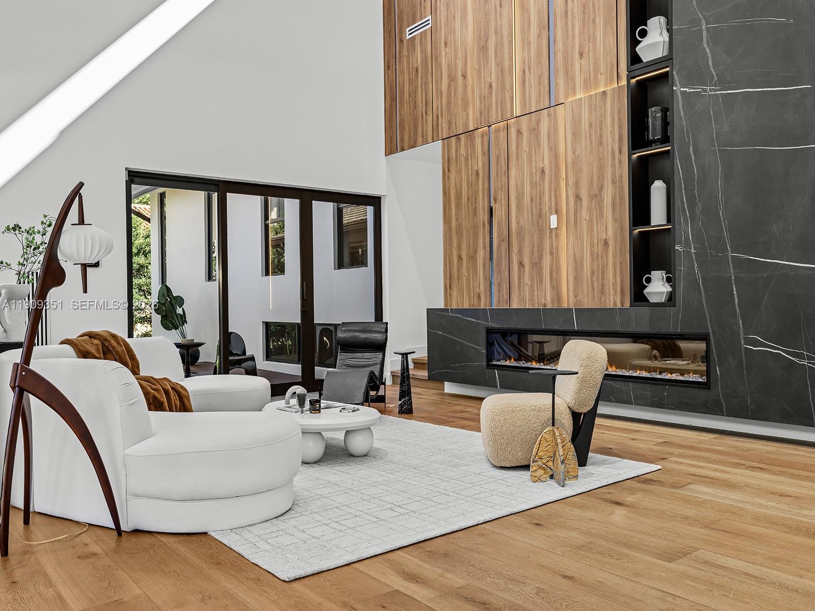A modern living room features a double-height ceiling, wood paneling, and a black marble fireplace — 7910 Los Pinos Cir, Coral Gables FL 33143, CORAL GABLES, FL