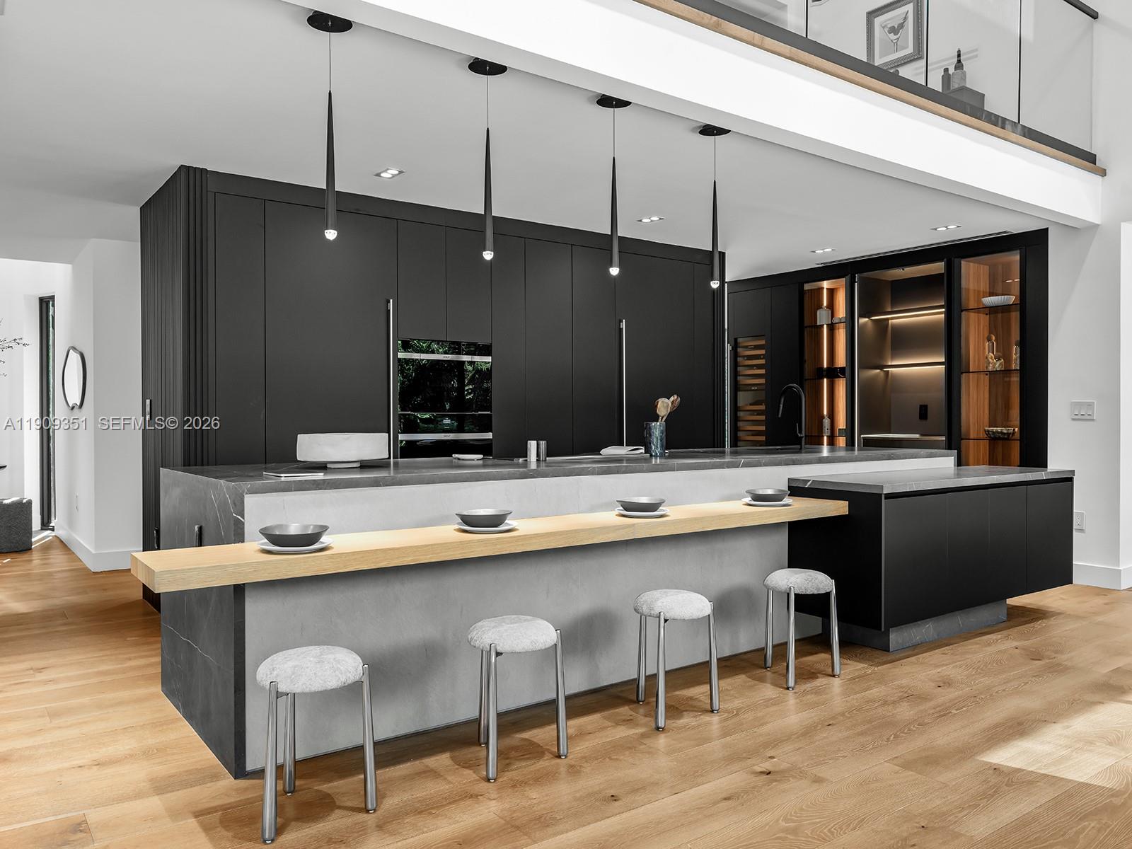 A modern kitchen features a large island with a wooden breakfast bar and four stools — 7910 Los Pinos Cir, Coral Gables FL 33143, CORAL GABLES, FL