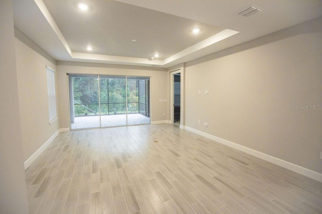 A bright, empty living room features light-colored tile flooring, a tray ceiling, and sliding glass doors — 4605 ROSATTI ROAD, WESLEY CHAPEL, FL