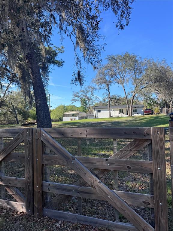 A wooden gate stands in the foreground before a house with a metal carport — 10731 LIBBY NUMBER 3 ROAD, CLERMONT, FL