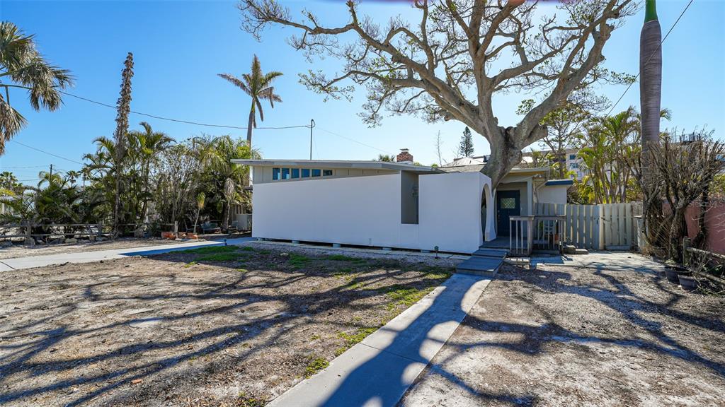 A white mid-century modern house with a large tree growing through the roof overhang — 132 HARRISON DRIVE, SARASOTA, FL