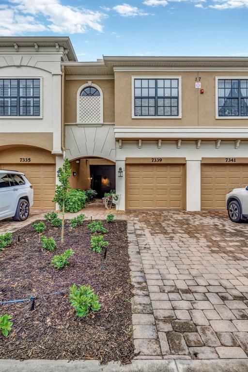The exterior of a multi-unit townhouse complex features beige stucco walls, arched entryways, and paved driveways — 7339 SKYBIRD ROAD UNIT 7339, BRADENTON, FL