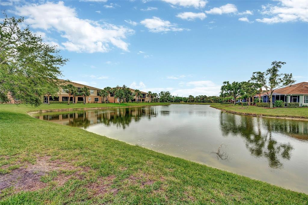 A pond sits between apartment buildings and residential homes under a blue sky — 7339 SKYBIRD ROAD UNIT 7339, BRADENTON, FL