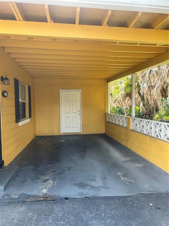 A yellow carport features a white door, concrete flooring, and a decorative concrete block wall — 2266 RAEFORD ROAD UNIT A6, ORLANDO, FL