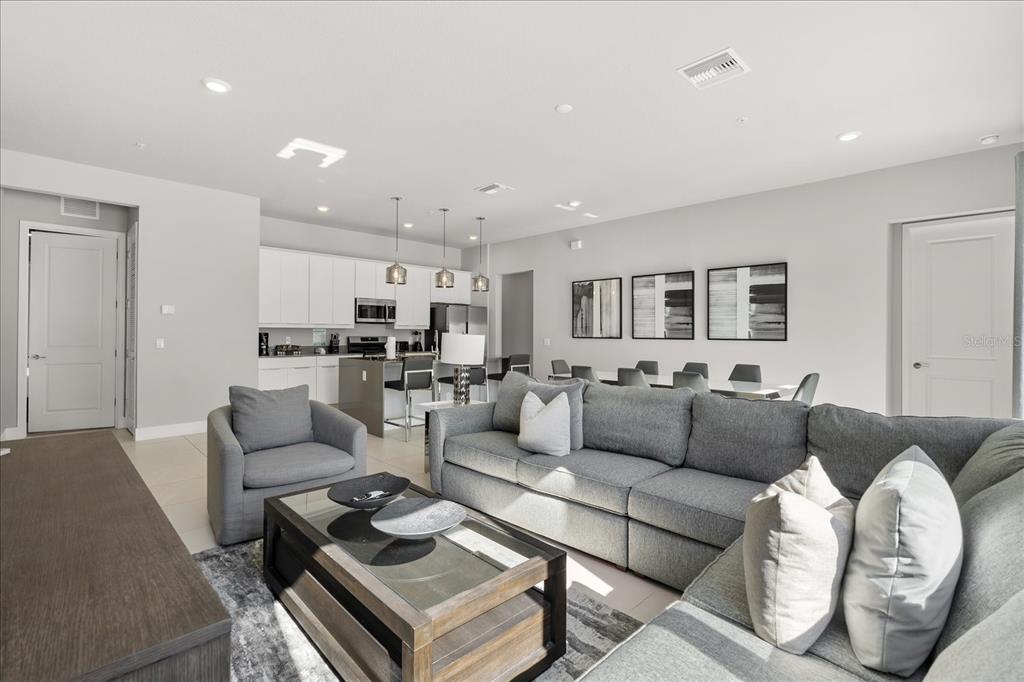 A modern open-concept living room features a gray sectional sofa, kitchen island, and dining area — 7760 SANDY RIDGE DRIVE UNIT 102, REUNION, FL