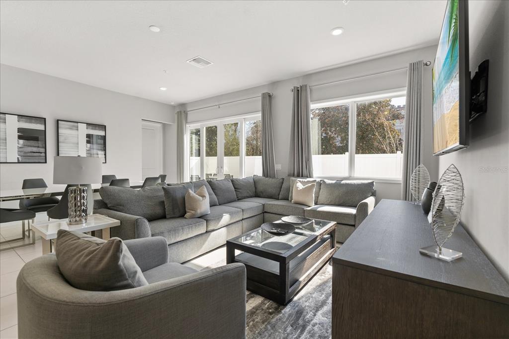 A living room features a gray sectional sofa, a glass-topped coffee table, and large windows — 7760 SANDY RIDGE DRIVE UNIT 102, REUNION, FL