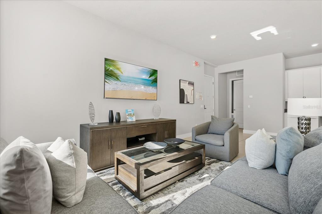 A living room features a grey sectional sofa, a coffee table, and a wall-mounted television — 7760 SANDY RIDGE DRIVE UNIT 102, REUNION, FL