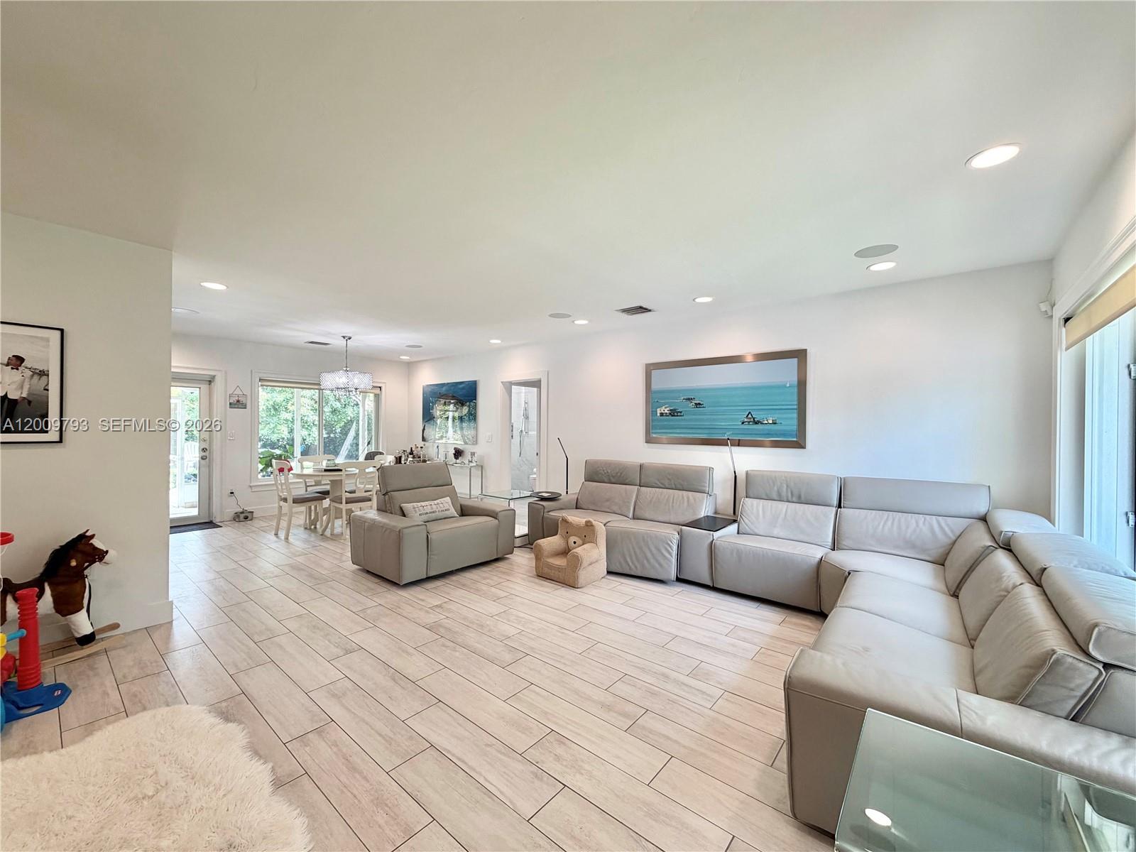 A spacious living room features light tile flooring, a large sectional sofa, and dining area — 823 NE 107th St, Biscayne Park FL 33161, BISCAYNE PARK, FL