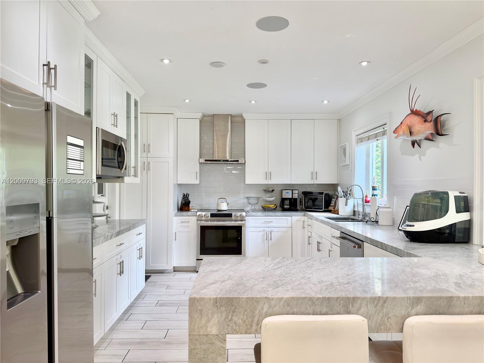 A modern white kitchen features marble countertops, stainless steel appliances, and a mounted fish display — 823 NE 107th St, Biscayne Park FL 33161, BISCAYNE PARK, FL