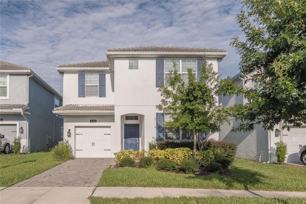 A two-story suburban house with a white stucco exterior, blue shutters, and a paved driveway — 1588 FLANGE DRIVE, DAVENPORT, FL